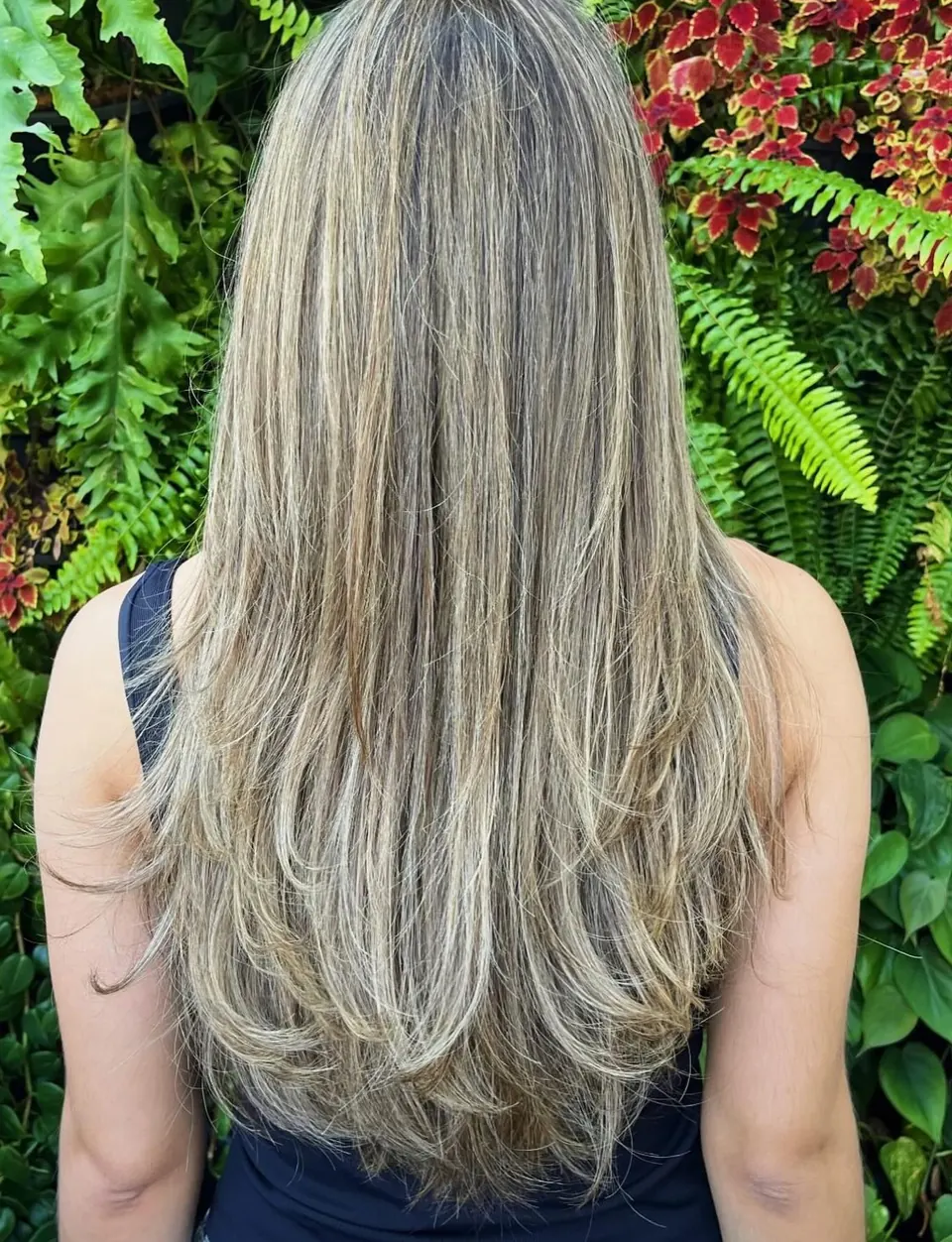 Cabelo longo repicado com luzes, cliente de costas, parede verde de plantas
