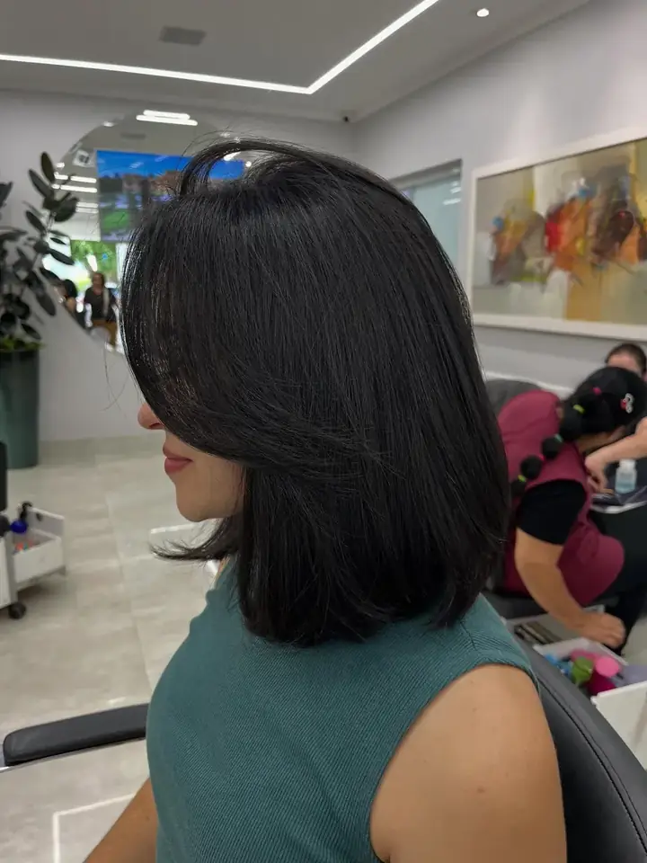 Cliente com corte chanel recebendo escova no salão, ambiente claro com luz de LED e plantas ao fundo