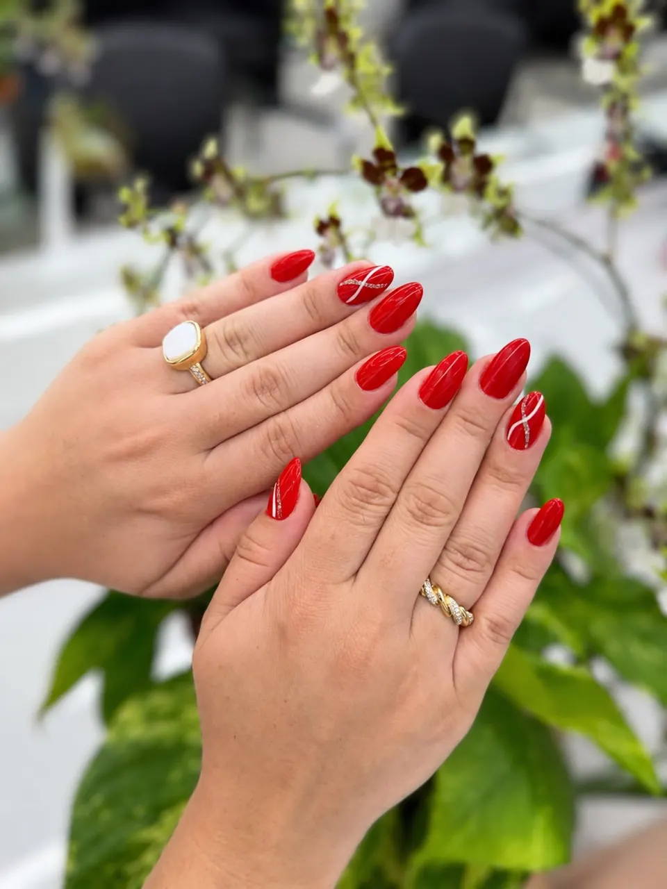 Unhas em gel vermelhas com detalhe em strass, mãos sobre fundo de flores